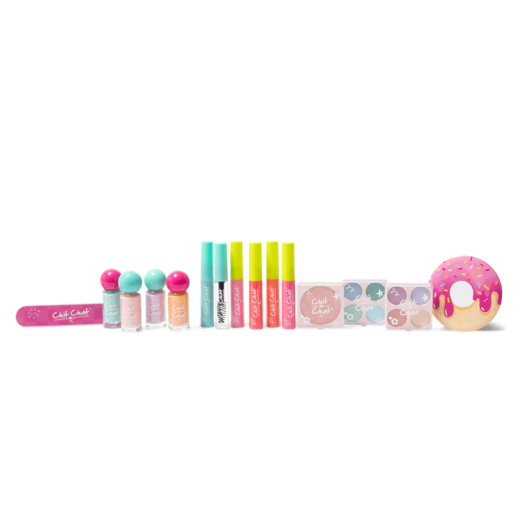 A Chit Chat makeup set arranged on a white background, featuring a pink nail file, small nail varnish bottles with colorful caps, lip gloss tubes, mascara tubes, eyeshadow palettes, blusher palettes and a donut-shaped cosmetic item.