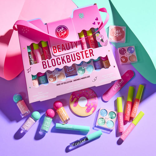 A pink Beauty Blockbuster makeup collection gift box displayed with various colourful makeup items including lip glosses, nail polishes, mascaras and face palettes on a vibrant purple and teal background.